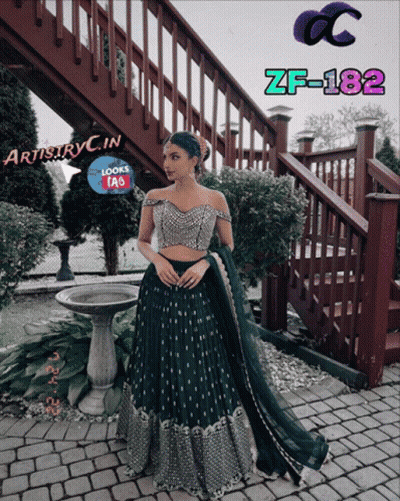 A Woman In A Green Dress Is Standing In Front Of A Staircase With Artistryc.in Written On The Bottom GIF