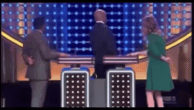 A Woman In A Green Dress Is Standing Next To A Man In A Suit GIF