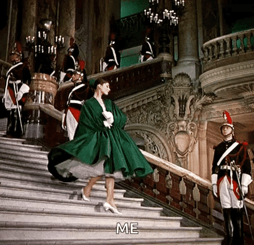 a woman in a green dress is walking down a set of stairs with soldiers behind her