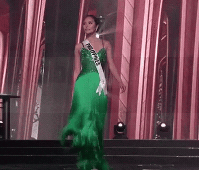 A Woman In A Green Dress Is Walking Down A Stage At A Pageant . GIF