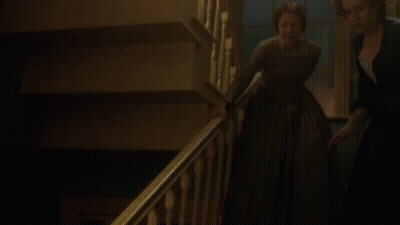 A Woman In A Green Dress Is Walking Down A Staircase GIF