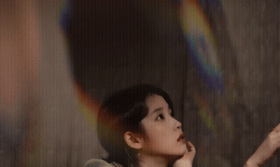 A Woman In A Green Dress Reaches For A Pink Rose GIF
