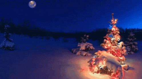 A Woman In A Green Dress Stands In Front Of A Snowy Christmas Tree GIF