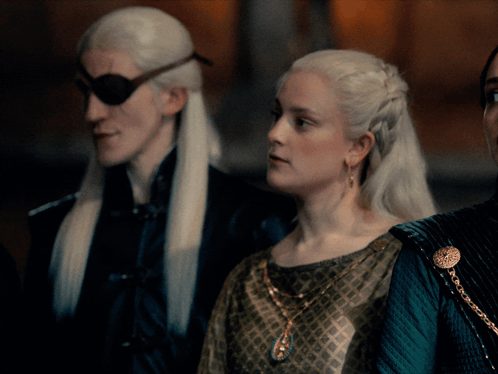 A Woman In A Green Dress Stands Next To A Man In A Black Jacket GIF