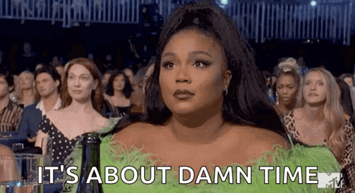 A Woman In A Green Feathered Dress Is Sitting In A Crowd Of People At A Concert . GIF