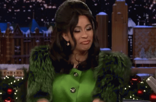 A Woman In A Green Fur Coat Is Smiling In Front Of Christmas Decorations GIF