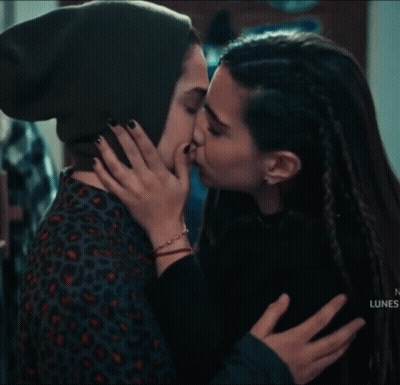 A Woman In A Green Hat Is Kissing Another Woman On The Forehead . GIF