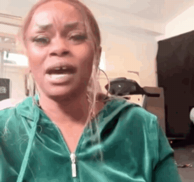 A Woman In A Green Hoodie Is Making A Funny Face While Standing In A Room . GIF