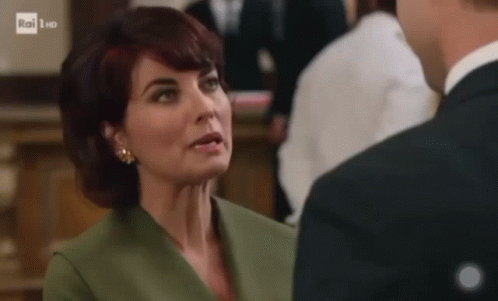 A Woman In A Green Jacket And Earrings Is Talking To A Man In A Suit . GIF