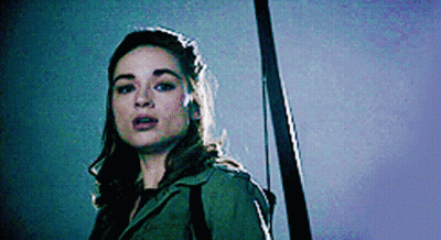 A Woman In A Green Jacket Is Holding A Sword . GIF