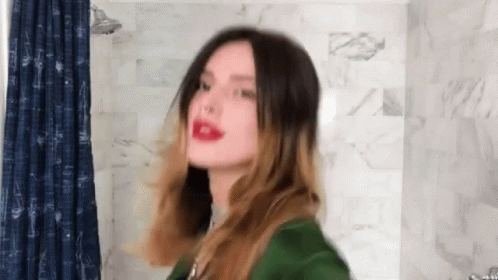 A Woman In A Green Jacket Is Standing In Front Of A Blue Shower Curtain GIF