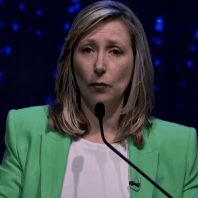 A Woman In A Green Jacket Is Talking Into A Microphone GIF