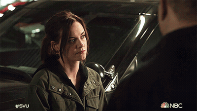 A Woman In A Green Jacket Is Talking To A Man In A Black Shirt In Front Of A Car That Says Nbc GIF
