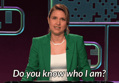 A Woman In A Green Jacket Stands Behind A Podium And Says Do You Know Who I Am GIF
