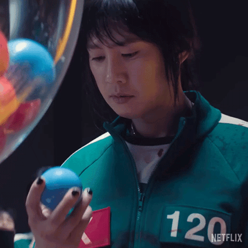 A Woman In A Green Jacket With The Number 120 On The Back Is Holding A Blue Ball . GIF