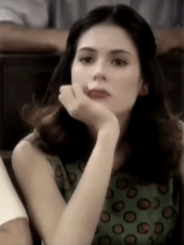 A Woman In A Green Polka Dot Dress Is Sitting In A Chair With Her Hand On Her Face . GIF