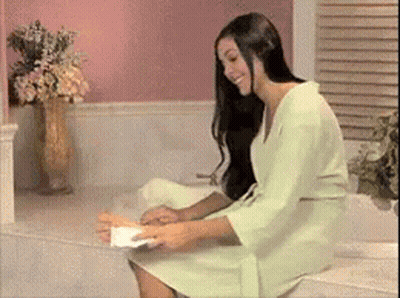 A Woman In A Green Robe Is Sitting On A Toilet Holding A Piece Of Toilet Paper GIF