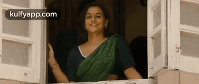 A Woman In A Green Sari Is Standing In A Window And Smiling . GIF