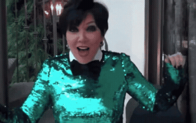A Woman In A Green Sequined Top And Black Bow Tie Is Sitting On A Couch . GIF