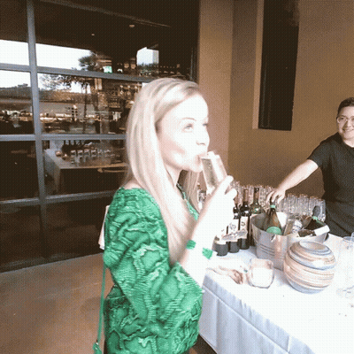 A Woman In A Green Shirt Drinks From A Glass GIF