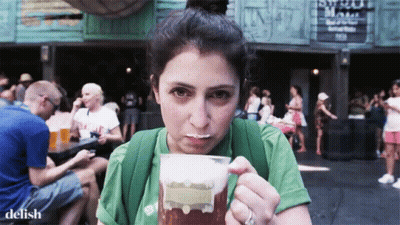 A Woman In A Green Shirt Is Drinking A Beer From A Plastic Cup GIF
