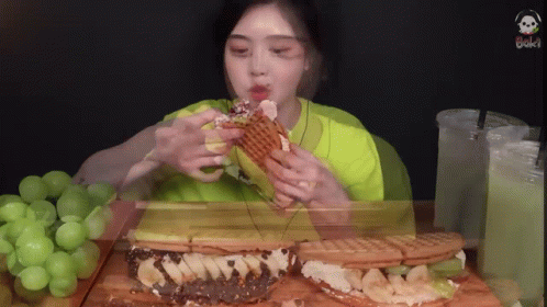 A Woman In A Green Shirt Is Eating A Sandwich With Bananas On It GIF