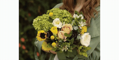 A Woman In A Green Shirt Is Holding A Bouquet Of Flowers . GIF