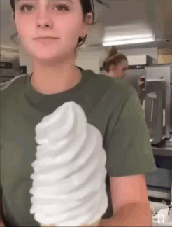 A Woman In A Green Shirt Is Holding A Giant Ice Cream Cone GIF