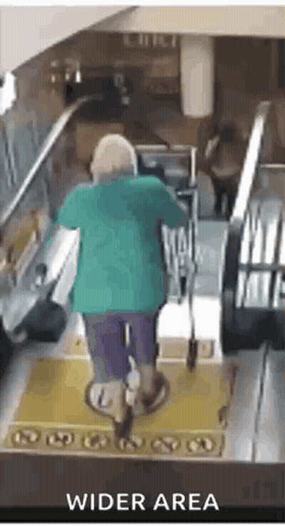 A Woman In A Green Shirt Is Riding An Escalator In A Wider Area GIF