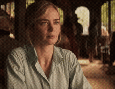 A Woman In A Green Shirt Is Sitting At A Table And Looking At The Camera GIF