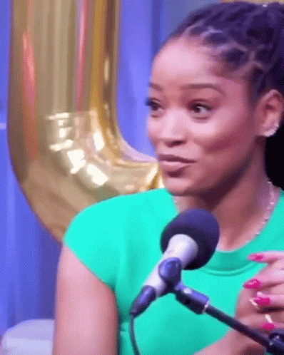 A Woman In A Green Shirt Is Sitting In Front Of A Microphone With Balloons In The Background . GIF