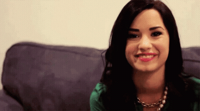 A Woman In A Green Shirt Is Sitting On A Couch Smiling . GIF