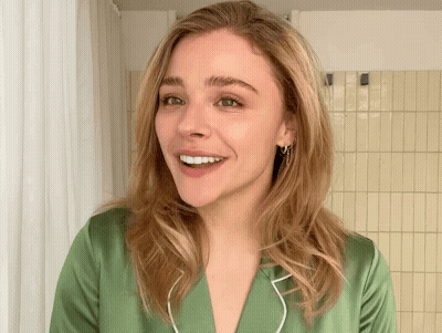 A Woman In A Green Shirt Is Smiling In Front Of A Yellow Tiled Wall GIF