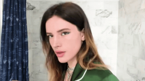 A Woman In A Green Shirt Is Standing In A Bathroom GIF
