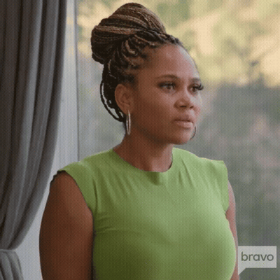 A Woman In A Green Shirt Is Standing In Front Of A Window With A Bravo Logo In The Corner GIF