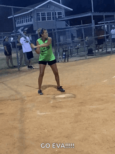 A Woman In A Green Shirt Is Swinging A Bat At A Ball GIF