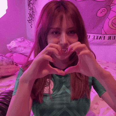 A Woman In A Green Shirt Makes A Heart Shape GIF