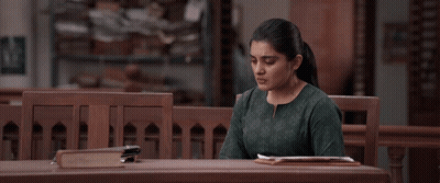 A Woman In A Green Shirt Sits At A Wooden Table GIF