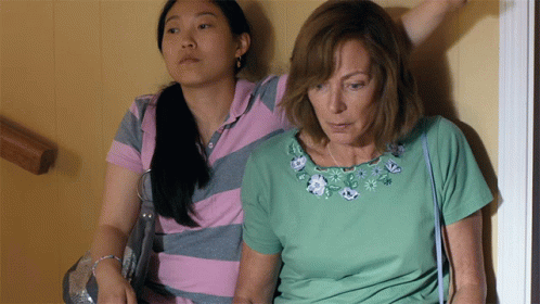 A Woman In A Green Shirt Sits Next To Another Woman In A Pink And Gray Striped Shirt GIF