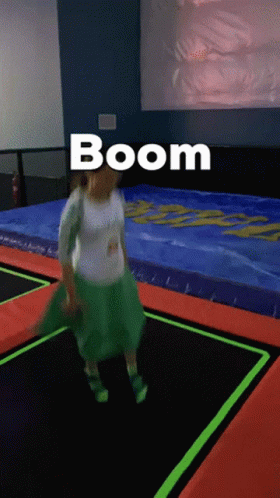 A Woman In A Green Skirt Is Jumping On A Trampoline And The Word Boom Is Above Her GIF