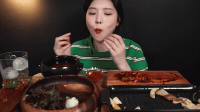 A Woman In A Green Striped Shirt Is Eating A Bowl Of Food GIF