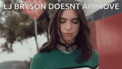 A Woman In A Green Sweater Is Standing In Front Of A Red Sign That Says " Lj Bryson Doesnt Approve " GIF