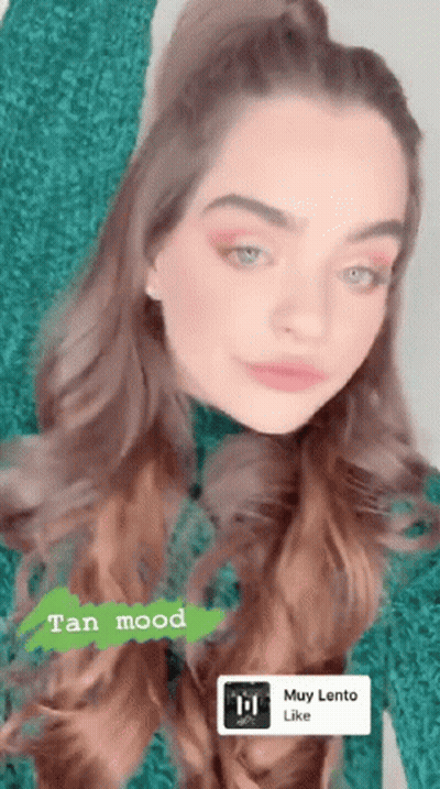 A Woman In A Green Sweater With A Tan Mood Sticker On Her Face GIF