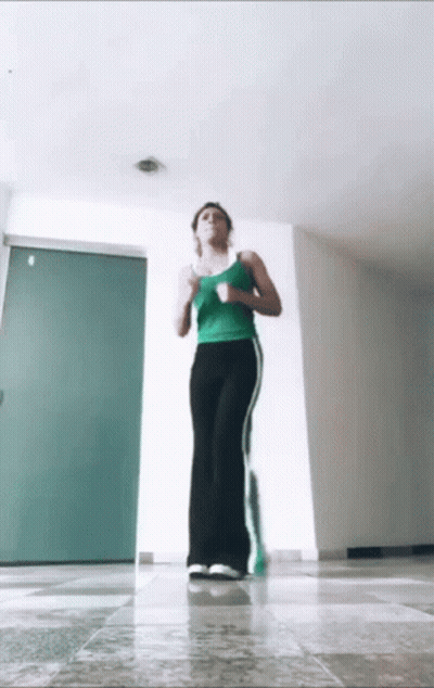 A Woman In A Green Tank Top And Black Pants Is Jogging GIF