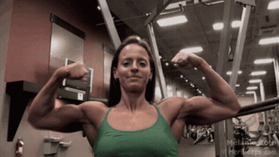 A Woman In A Green Tank Top Is Flexing Her Muscles In A Gym .. GIF