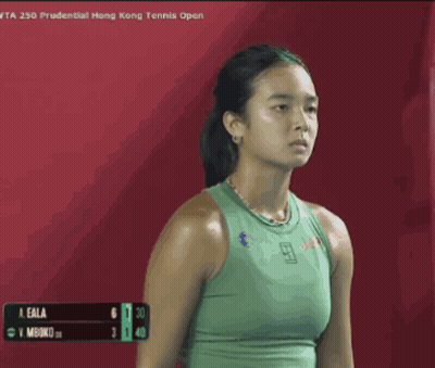 A Woman In A Green Tank Top Is Standing In Front Of A Red Background . GIF