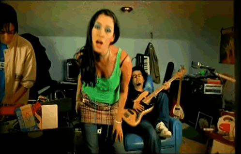 A Woman In A Green Tank Top Stands In Front Of A Man Playing A Guitar GIF