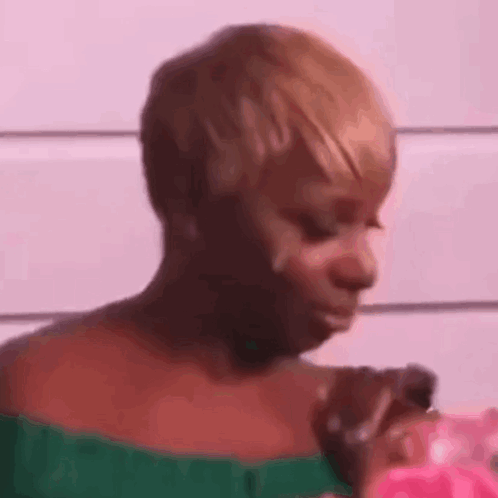 A Woman In A Green Top Is Holding A Pink Object In Her Hand And Making A Funny Face . GIF