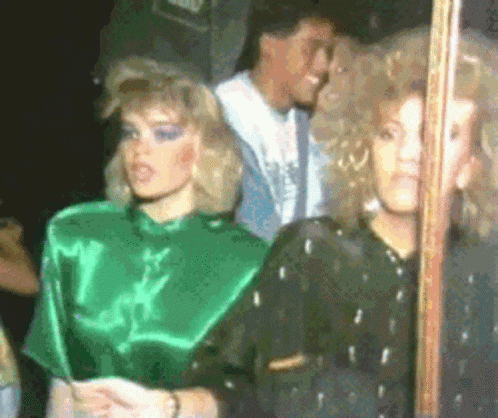 A Woman In A Green Top Is Standing Next To Another Woman In A Black Dress . GIF