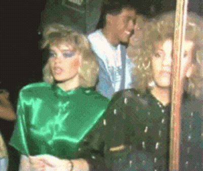 A Woman In A Green Top Stands Next To Another Woman In A Black Top GIF